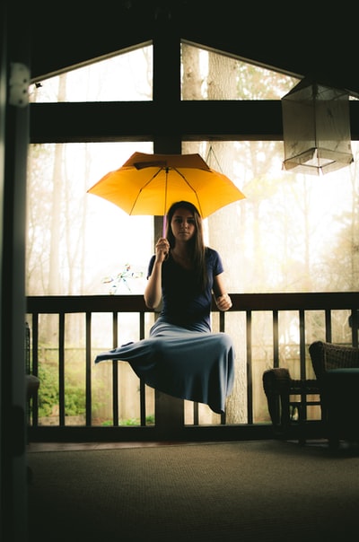 一个穿着灰色衣服的女人坐在棕色的木椅上，手里拿着雨伞